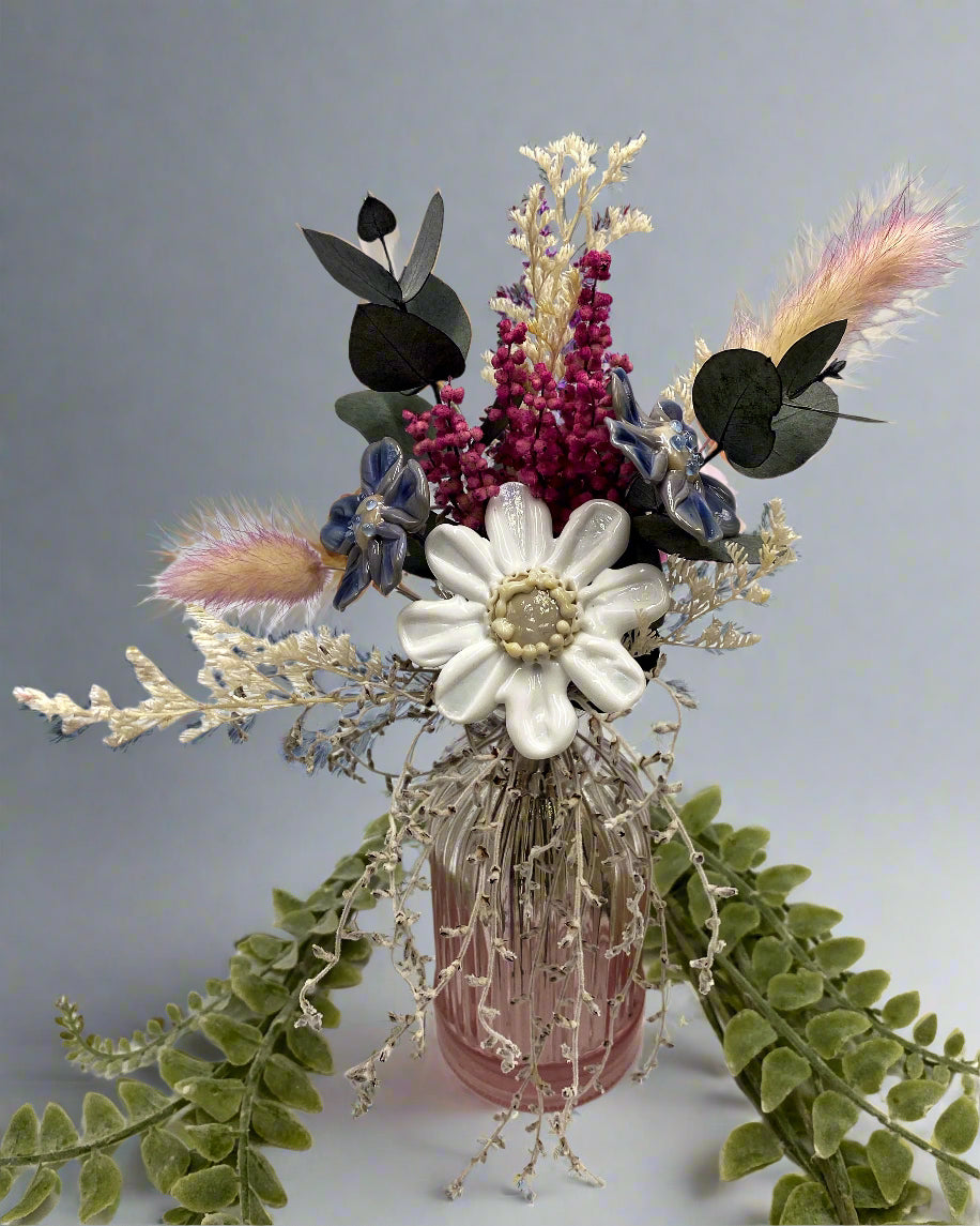 Decorative floral arrangement with a white flower, pink and purple elements, and green leaves on a light background.