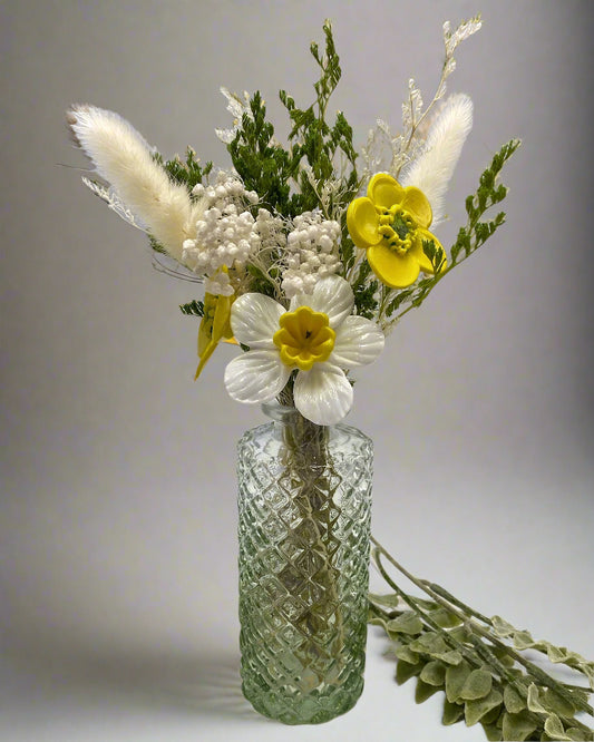 Decorative floral arrangement with yellow and white flowers in a textured glass vase on a light background